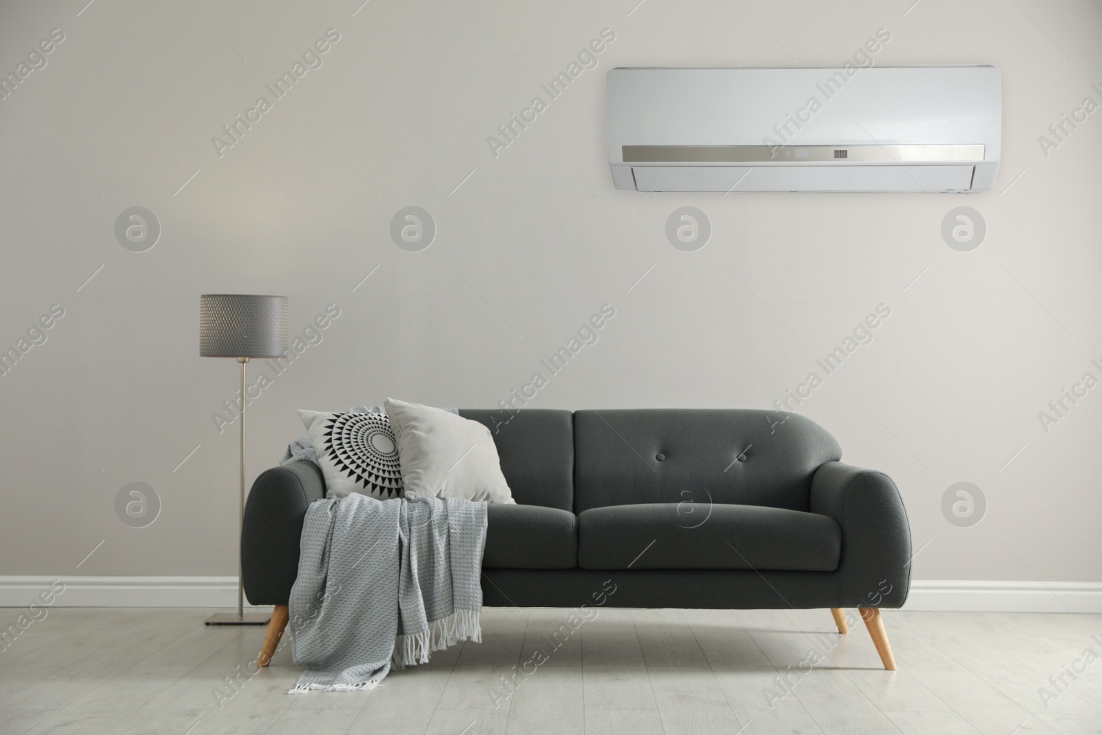 Image of Modern air conditioner on white wall in room with stylish grey sofa