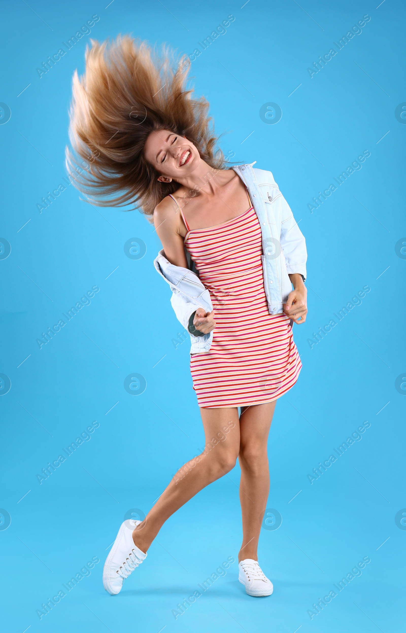 Photo of Beautiful young woman in dress and jacket dancing on blue background
