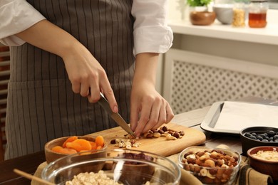 Photo of Making granola. Woman cutting nuts at table in kitchen, closeup