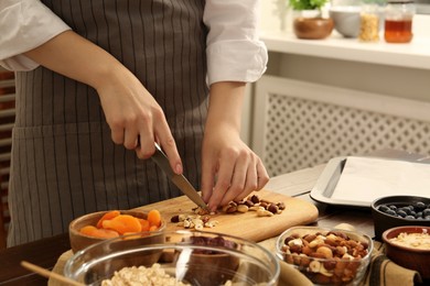 Making granola. Woman cutting nuts at table in kitchen, closeup