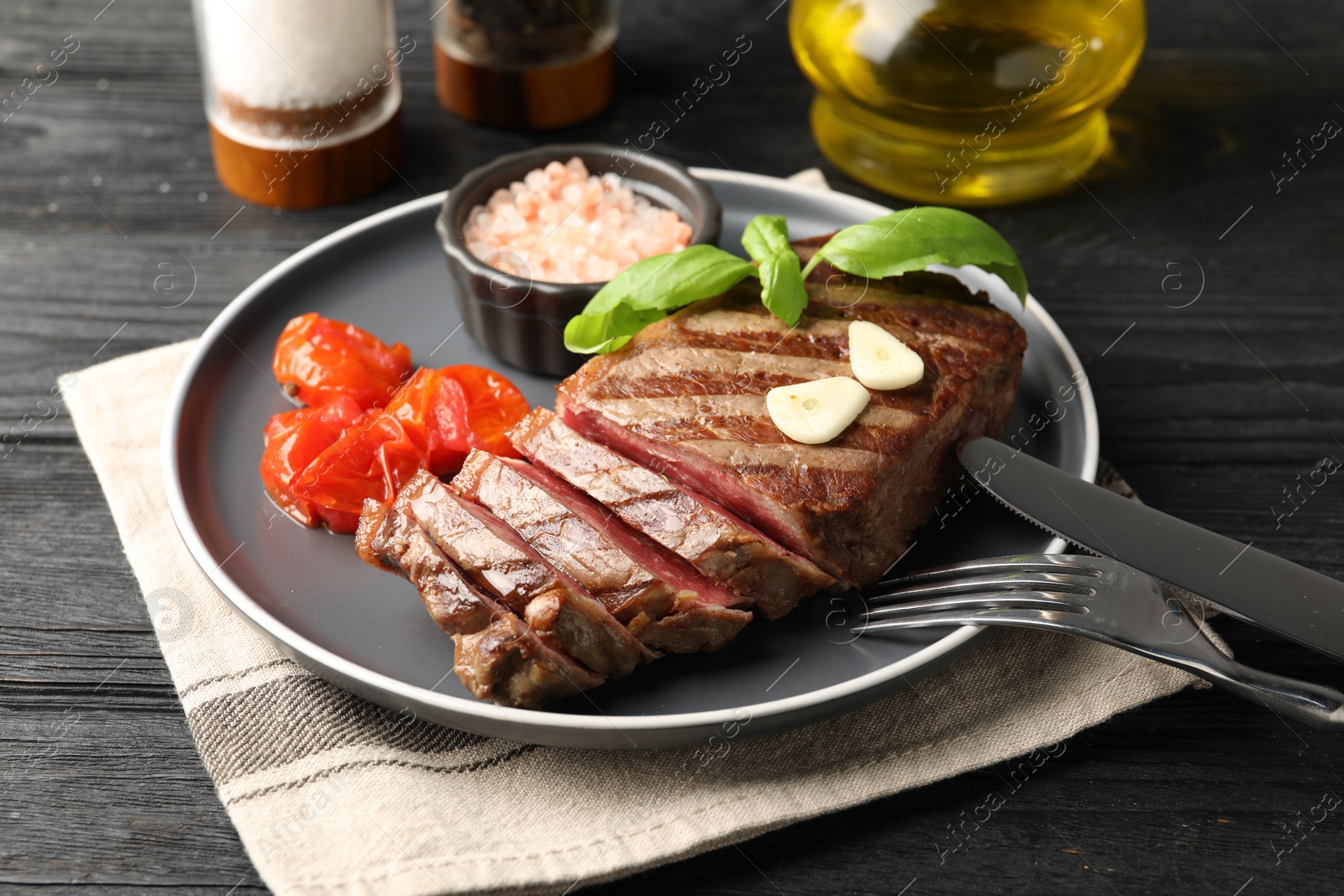 Photo of Delicious grilled beef steak served with spices and tomatoes on table