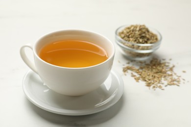 Photo of Fennel tea in cup and seeds on white marble table, closeup