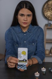 Photo of Fortune teller with tarot card Ace of Pentacles at grey table indoors