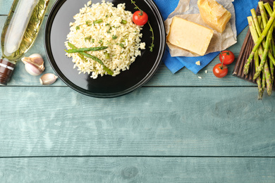 Photo of Delicious risotto with asparagus served on blue wooden table, flat lay. Space for text