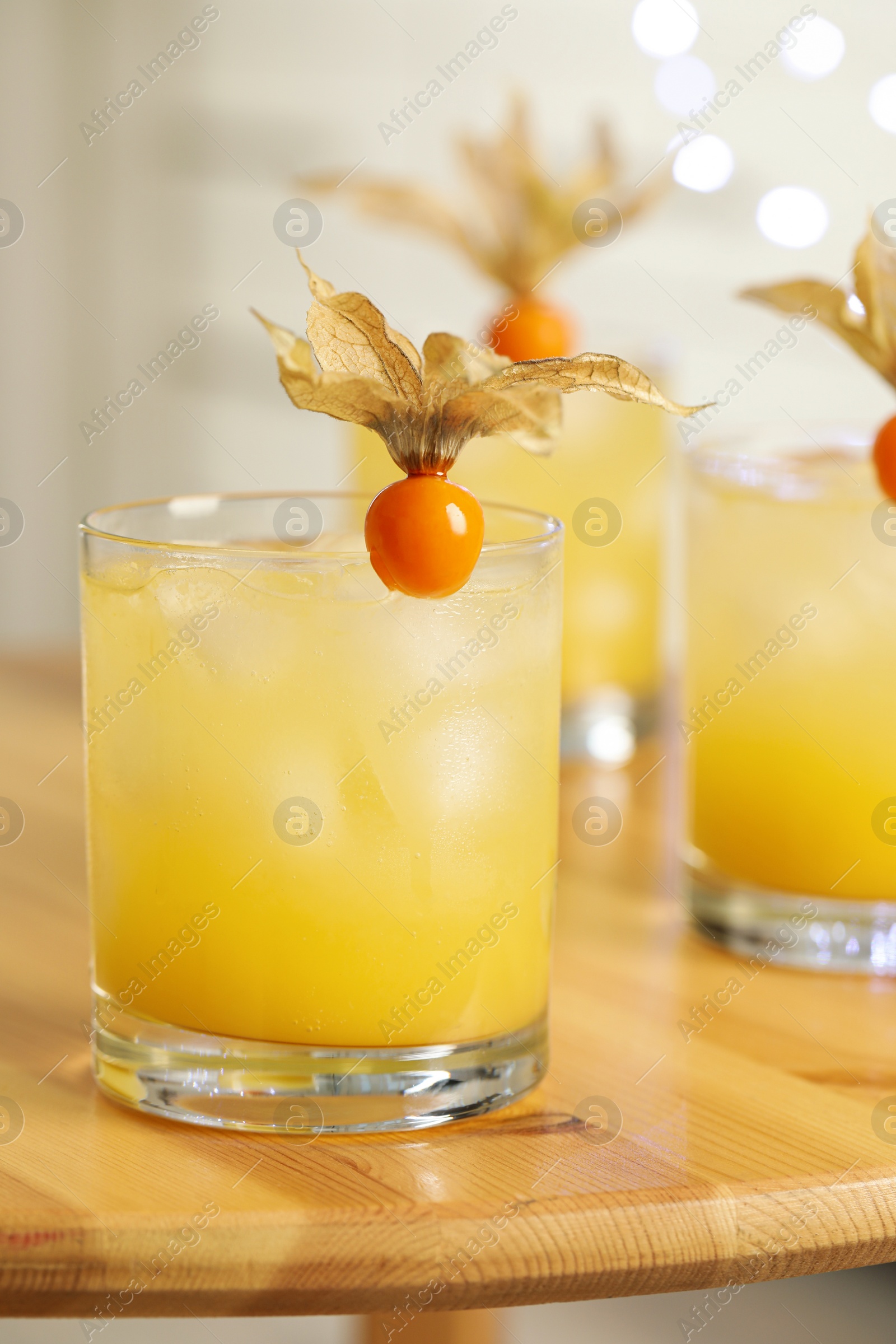 Photo of Refreshing cocktails decorated with physalis fruits on wooden table against blurred festive lights