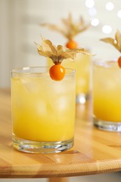 Refreshing cocktails decorated with physalis fruits on wooden table against blurred festive lights