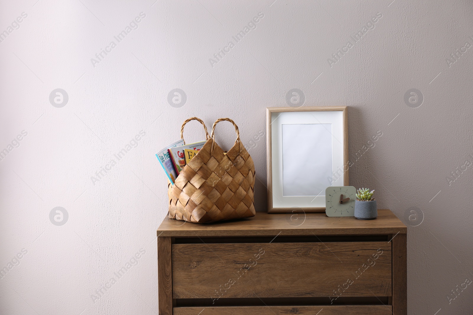 Photo of Wooden chest of drawers with stylish bag, decor and empty frame near light wall in room. Interior design