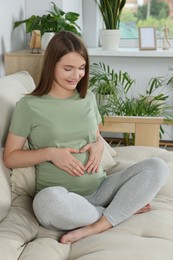 Photo of Happy pregnant woman making heart with her hands in living room