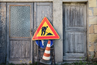 Photo of Different traffic signs and road safety cone near wooden door of old house