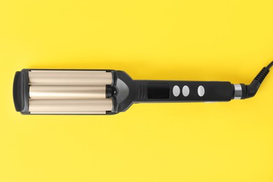 Photo of Modern triple curling iron on yellow background, top view
