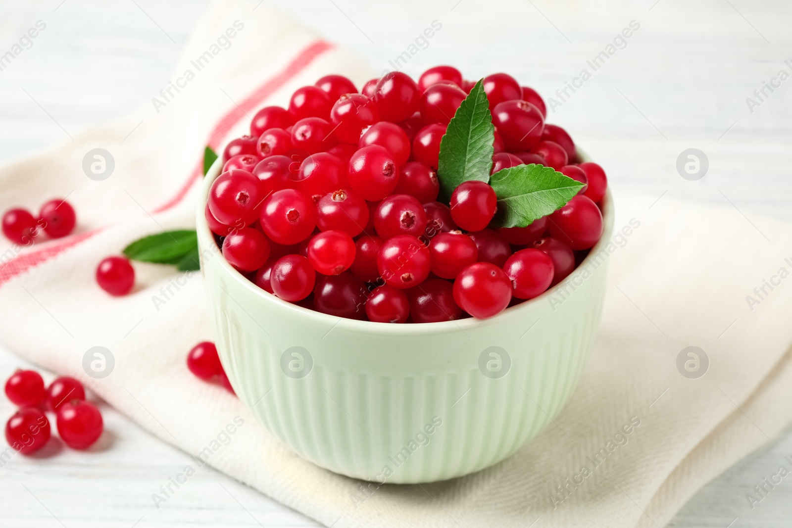 Photo of Tasty ripe cranberries and green leaves on white table, closeup