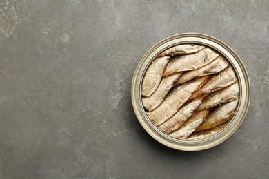 Photo of Sprats in tin can on grey textured table, top view. Space for text
