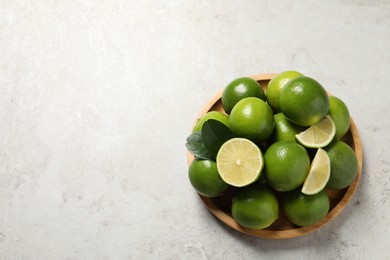 Photo of Fresh ripe limes and green leaves on light table, top view. Space for text