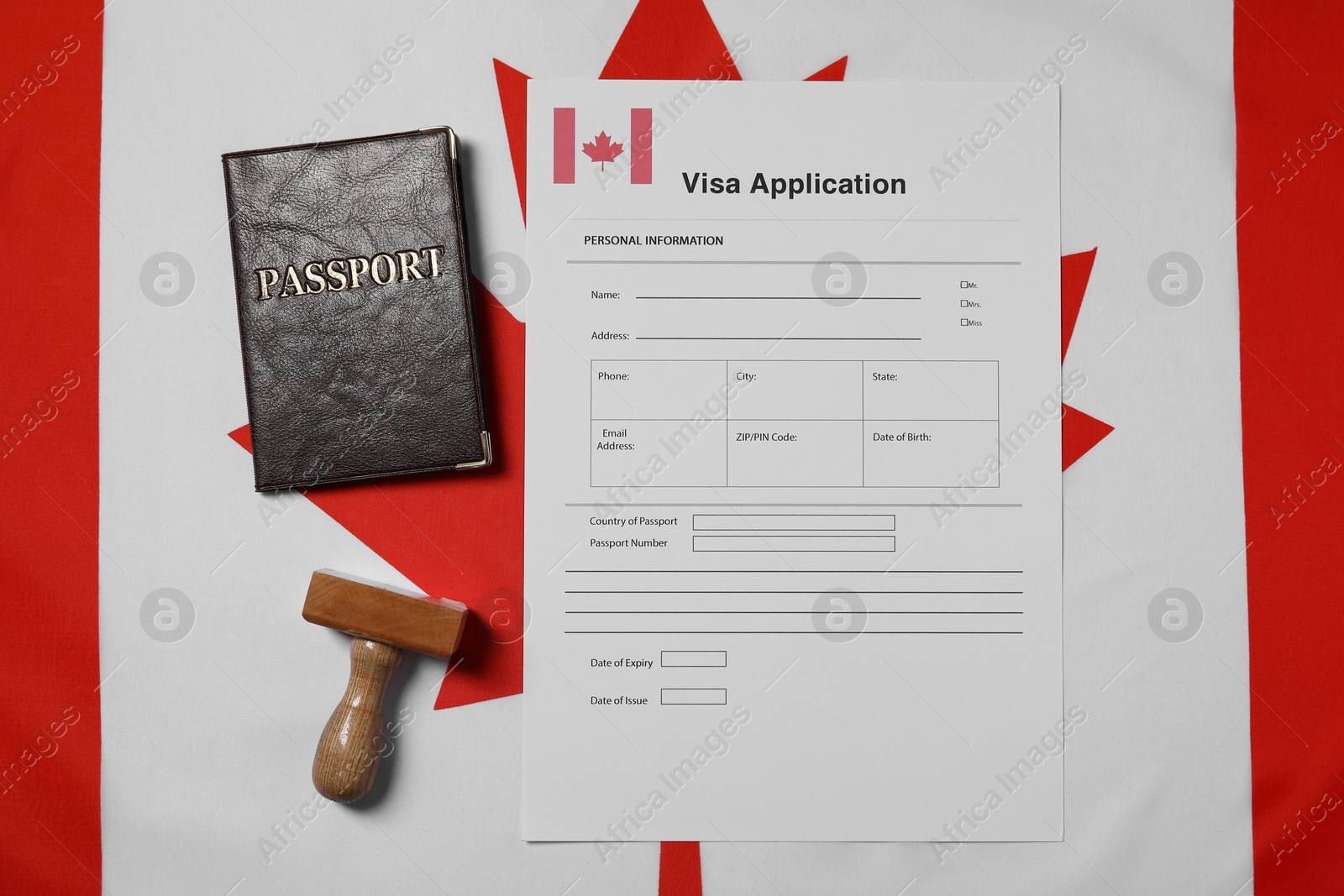 Photo of Immigration to Canada. Visa application form, wooden stamp and passport on flag, flat lay
