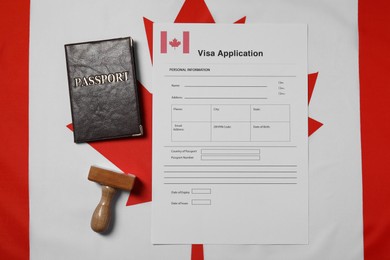 Photo of Immigration to Canada. Visa application form, wooden stamp and passport on flag, flat lay