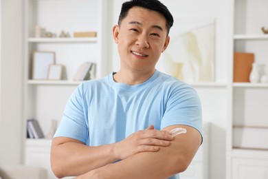 Photo of Handsome man applying body cream onto his arm indoors