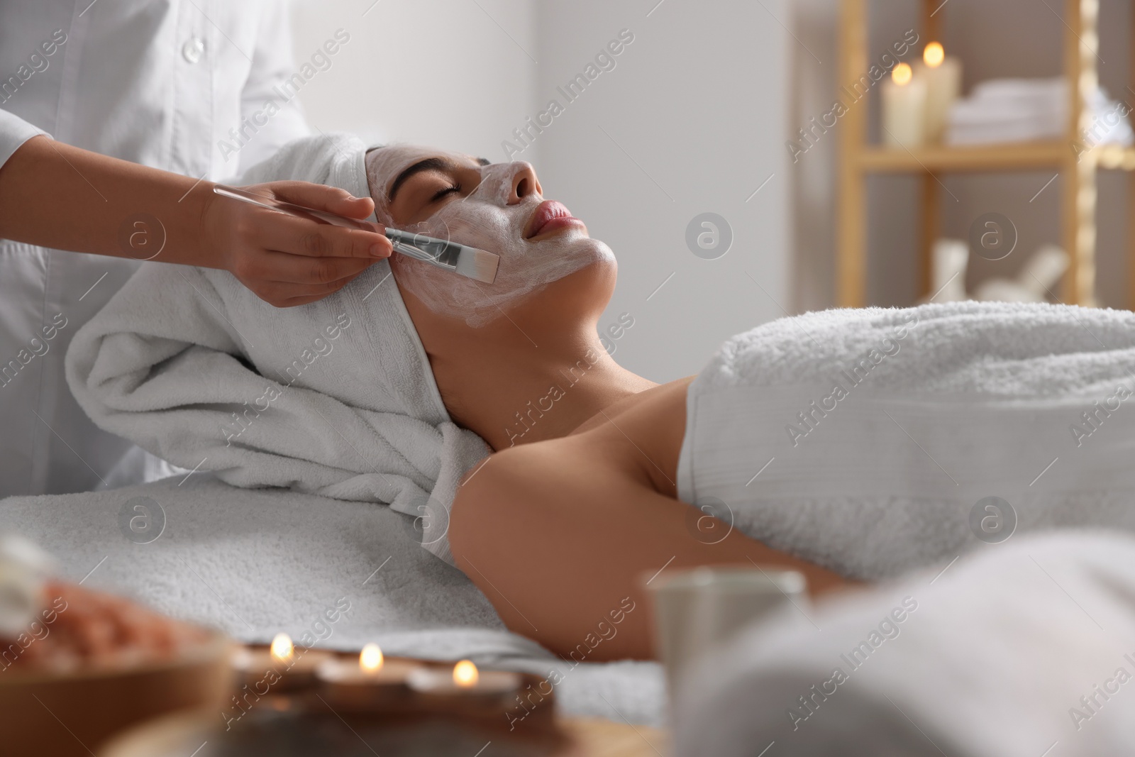 Photo of Cosmetologist applying mask on woman's face in spa salon, closeup