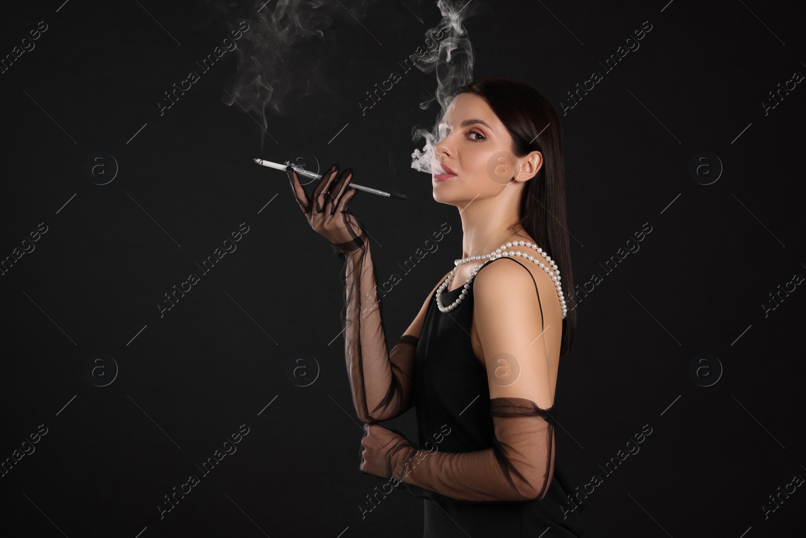 Photo of Woman using long cigarette holder for smoking on black background, space for text