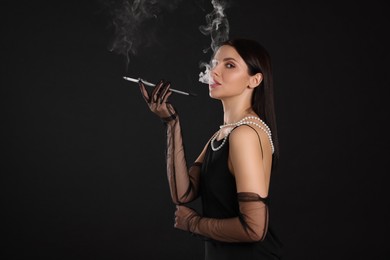 Photo of Woman using long cigarette holder for smoking on black background, space for text