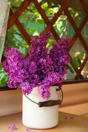 Photo of Beautiful lilac flowers in milk can on wooden table indoors