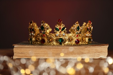 Photo of Beautiful golden crown, old book and fairy lights on brown background. Fantasy item