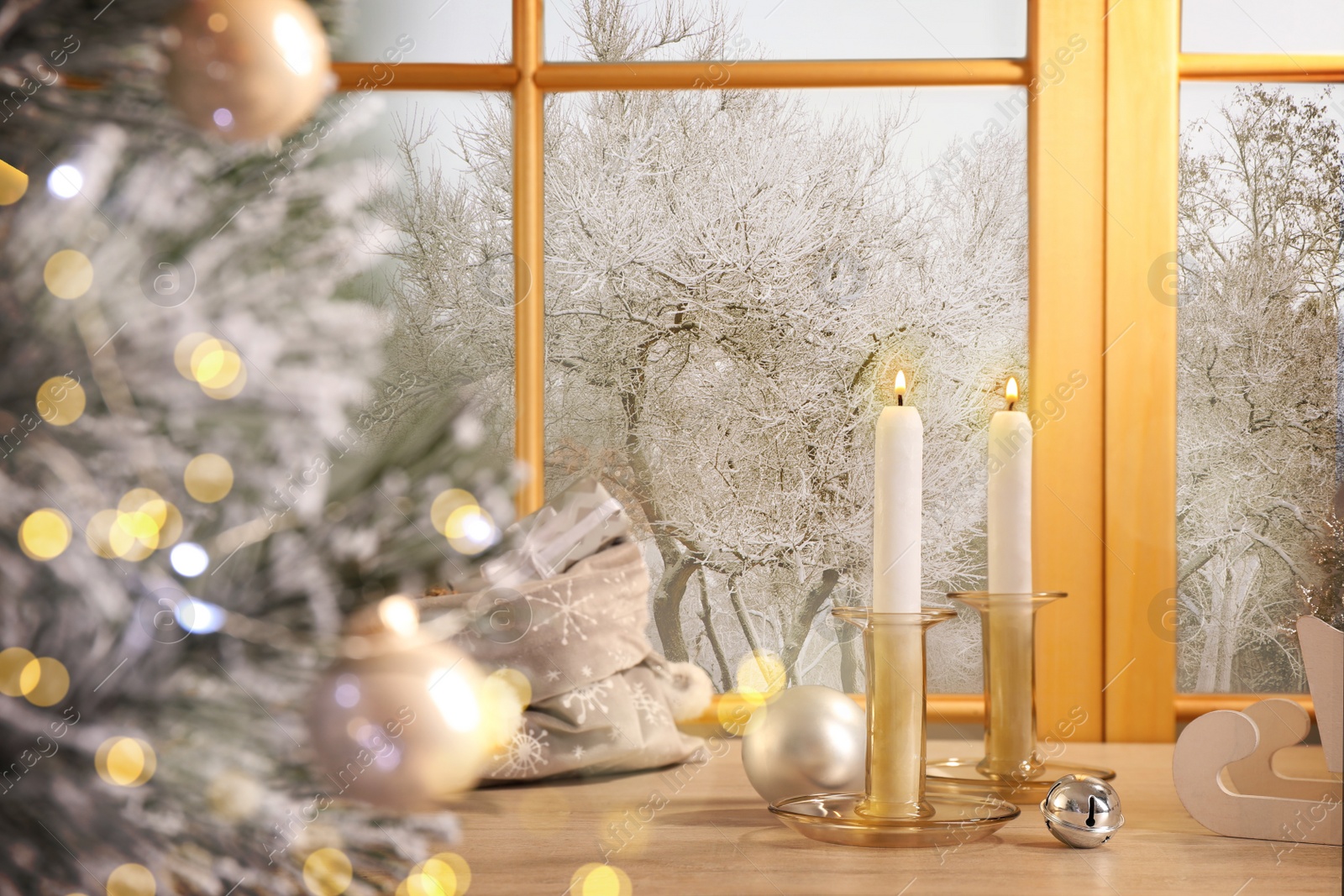 Image of Burning candles and festive decor on window sill near Christmas tree indoors