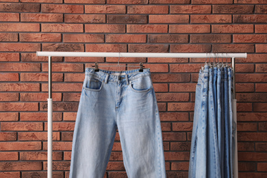 Photo of Rack with stylish jeans near brick wall, closeup