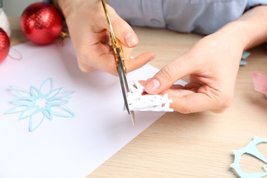 Woman making paper snowflake at wooden table, closeup