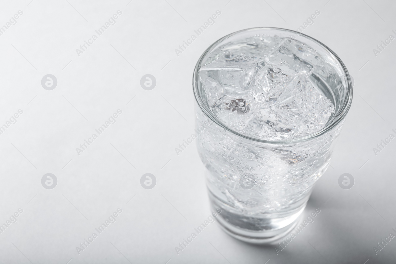 Photo of Glass of soda water with ice on light background. Space for text