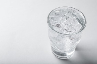 Photo of Glass of soda water with ice on light background. Space for text
