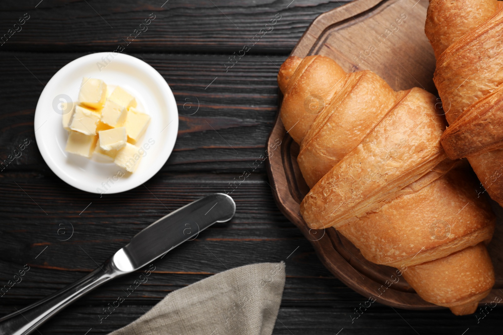 Photo of Tasty fresh croissants and butter on black wooden table, flat lay