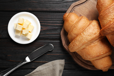 Tasty fresh croissants and butter on black wooden table, flat lay