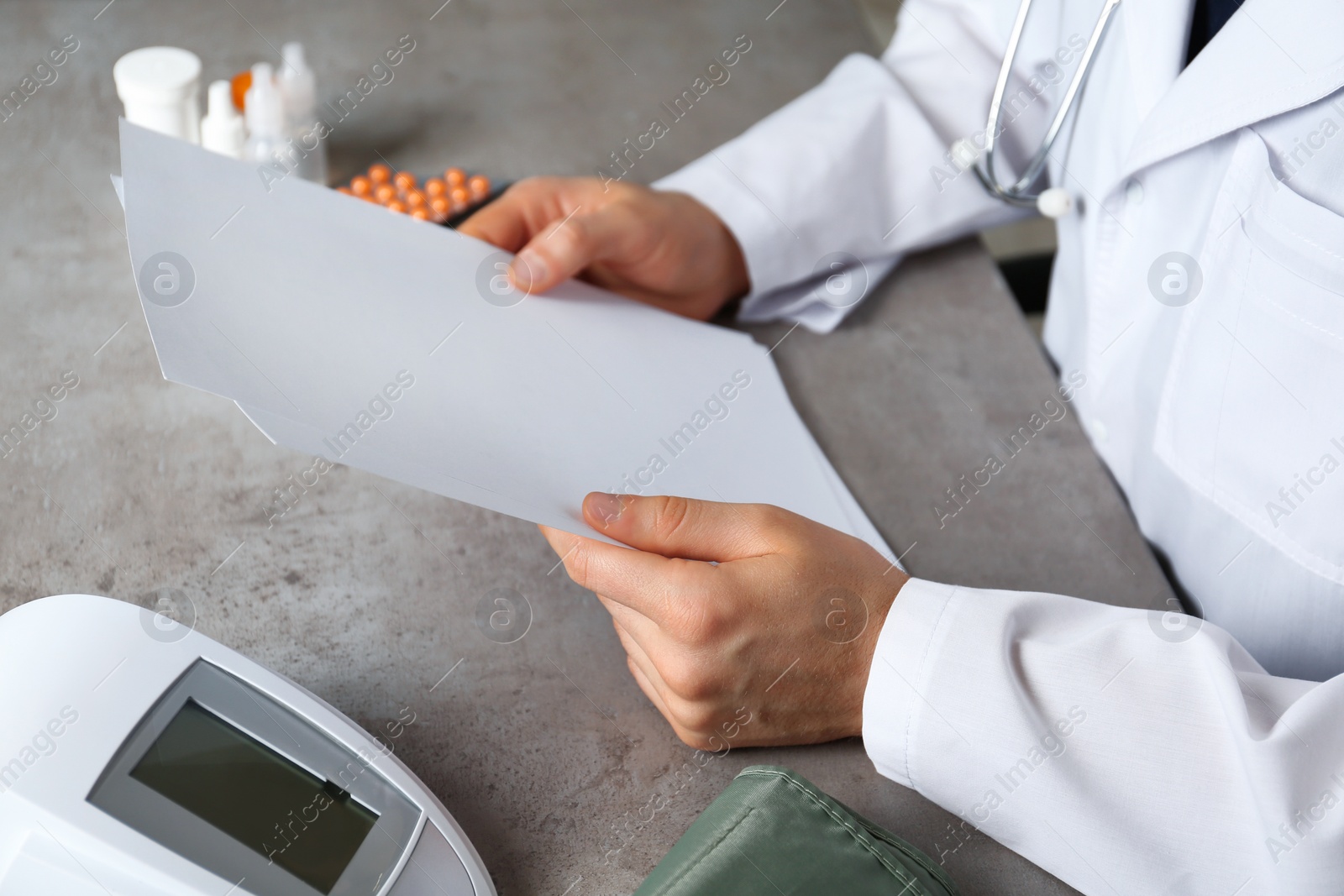 Photo of Doctor with papers and digital pressure meter at table, closeup with space for text. Medical objects