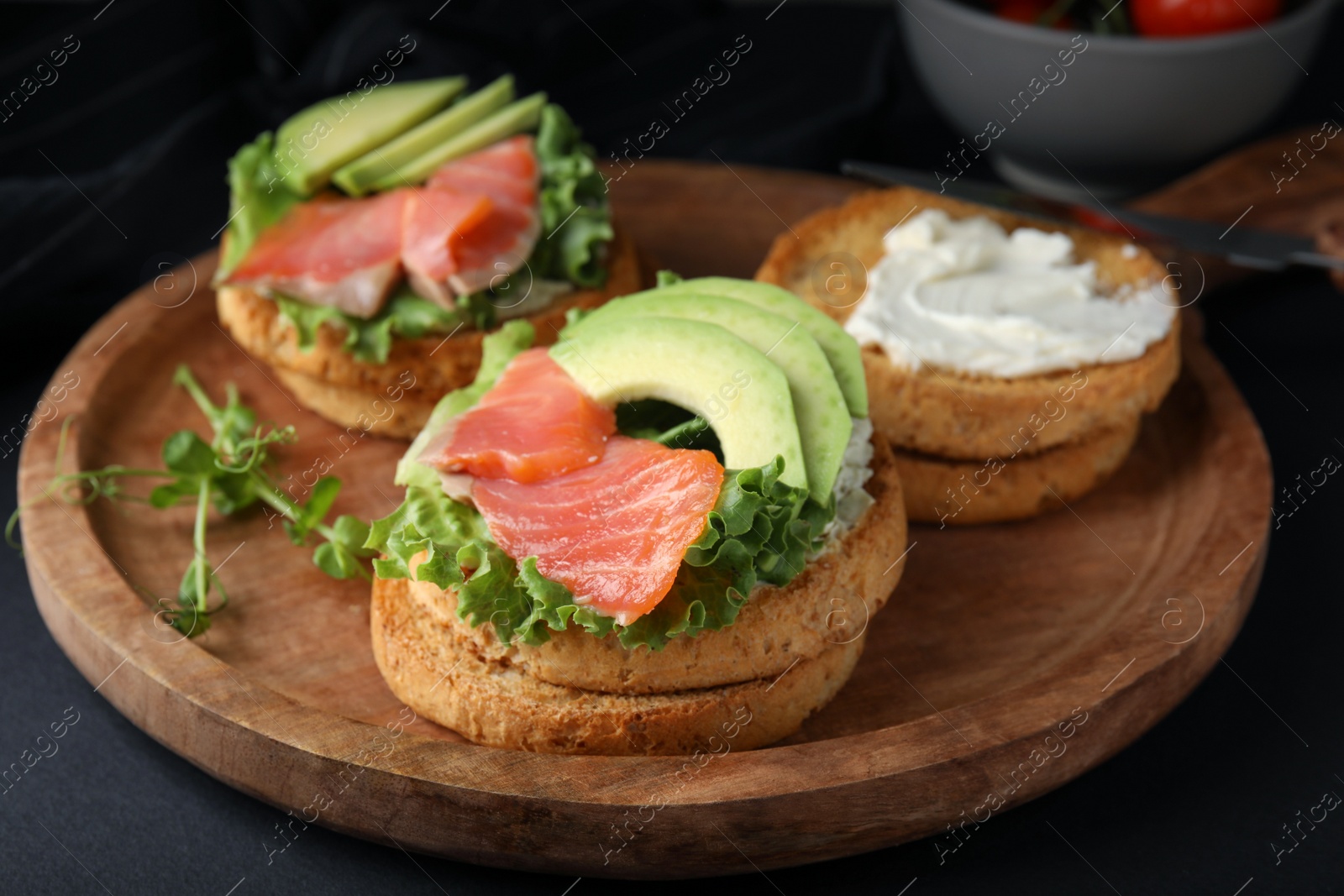 Photo of Tasty rusks with salmon, cream cheese and avocado served on black table, closeup