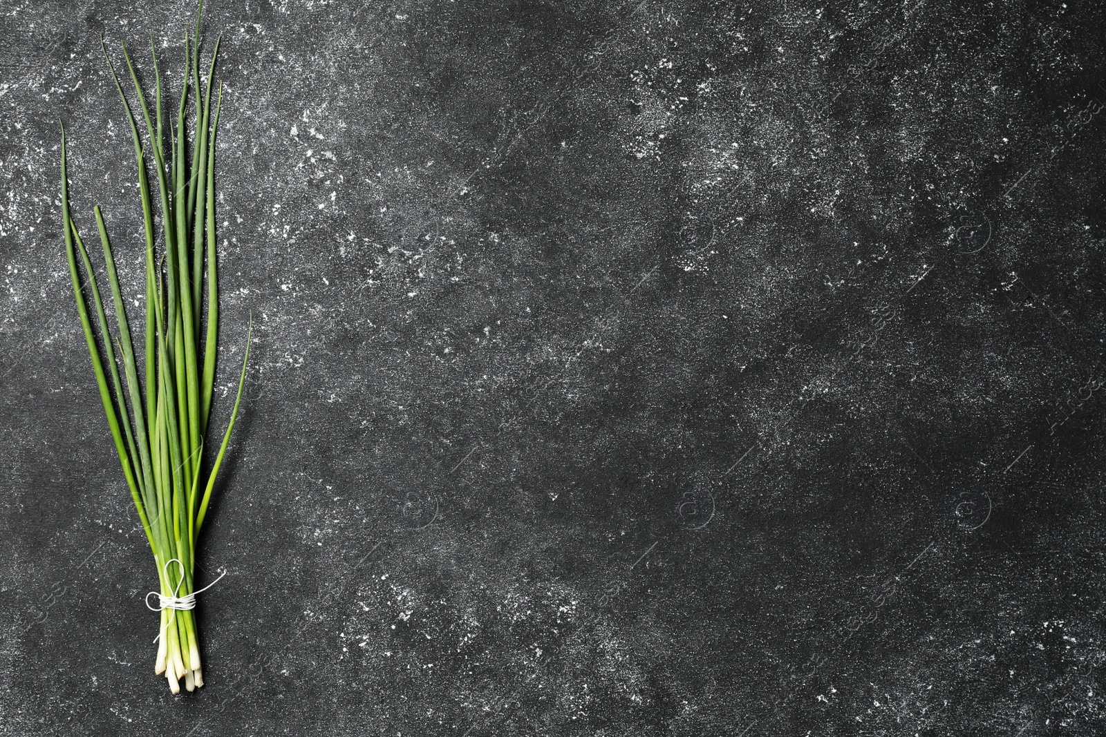 Photo of Bunch of fresh green onion on black table, top view. Space for text