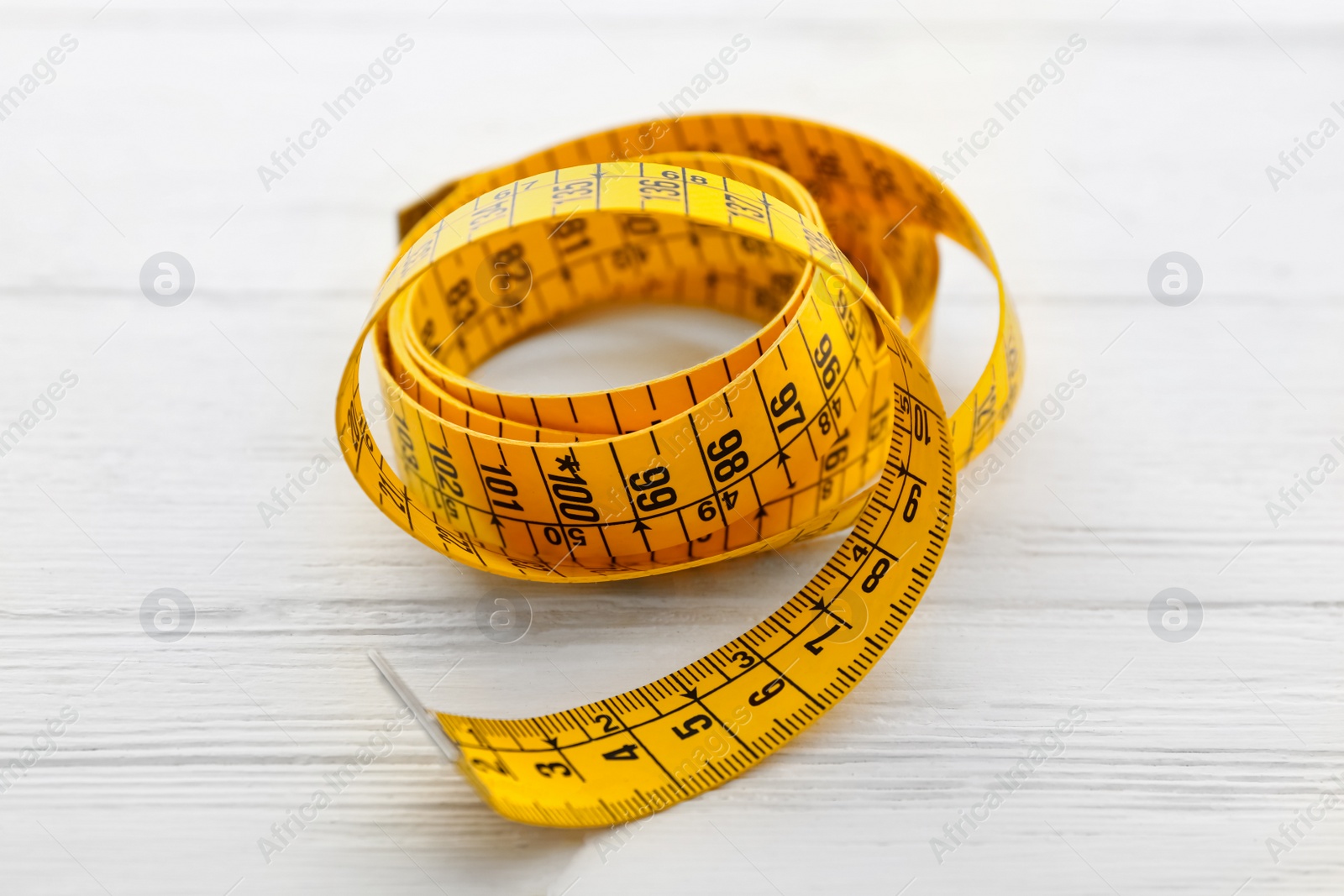 Photo of Yellow measuring tape on white wooden table, closeup