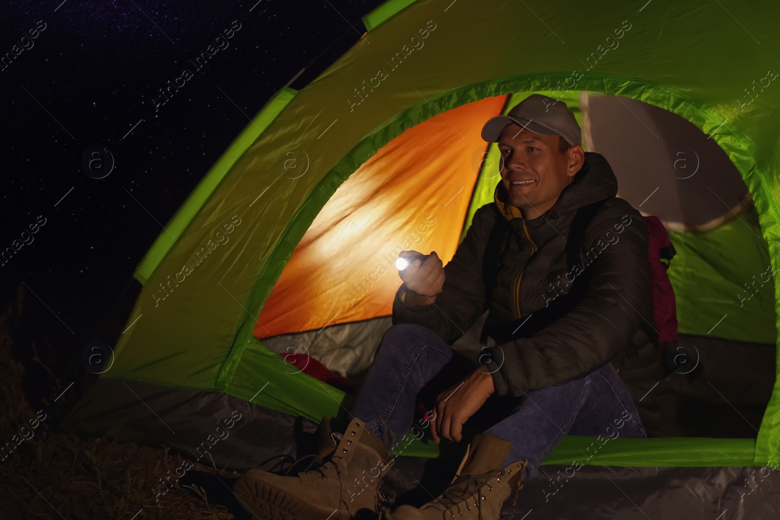 Photo of Man with flashlight sitting in tent at night