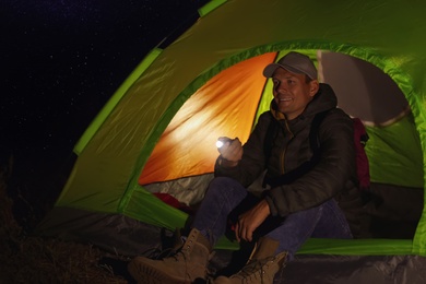 Photo of Man with flashlight sitting in tent at night