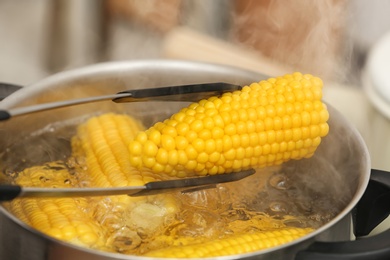 Photo of Taking corn cob from stewpot with boiling water, closeup