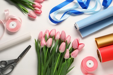 Photo of Making beautiful bouquet. Fresh pink tulips, ribbons, wrapping paper and scissors on white wooden table, flat lay