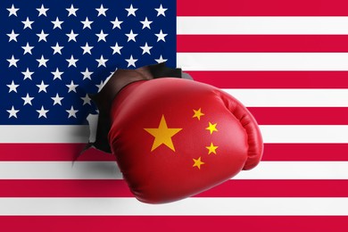Image of Man in boxing glove with Chinese flag punching hole through American flag, closeup. Trade war
