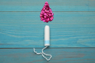 Photo of Tampon near drop made of pink sequins on turquoise wooden background, flat lay. Menstrual hygiene product