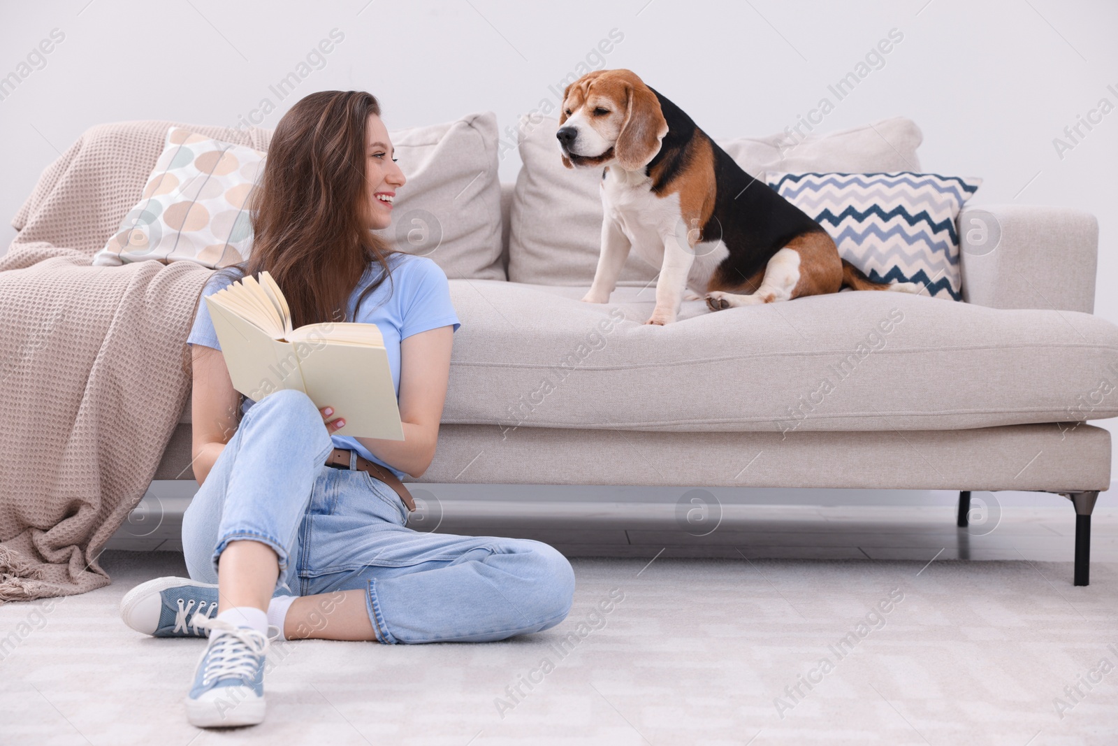 Photo of Happy young woman reading book near her cute Beagle dog at home. Lovely pet