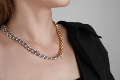 Photo of Woman wearing metal chain on light grey background, closeup. Luxury jewelry