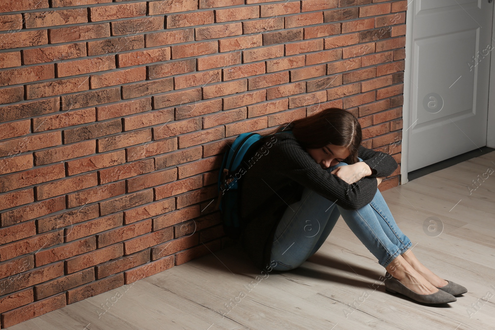 Photo of Upset teenage girl with backpack sitting on floor near wall. Space for text