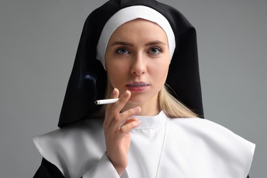 Woman in nun habit smoking cigarette on grey background