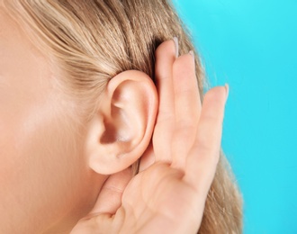 Photo of Young woman with hearing problem on color background, closeup