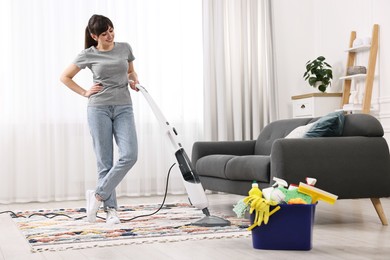 Happy young housewife vacuuming rug at home