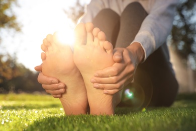 Young woman sitting barefoot on fresh green grass outdoors, closeup