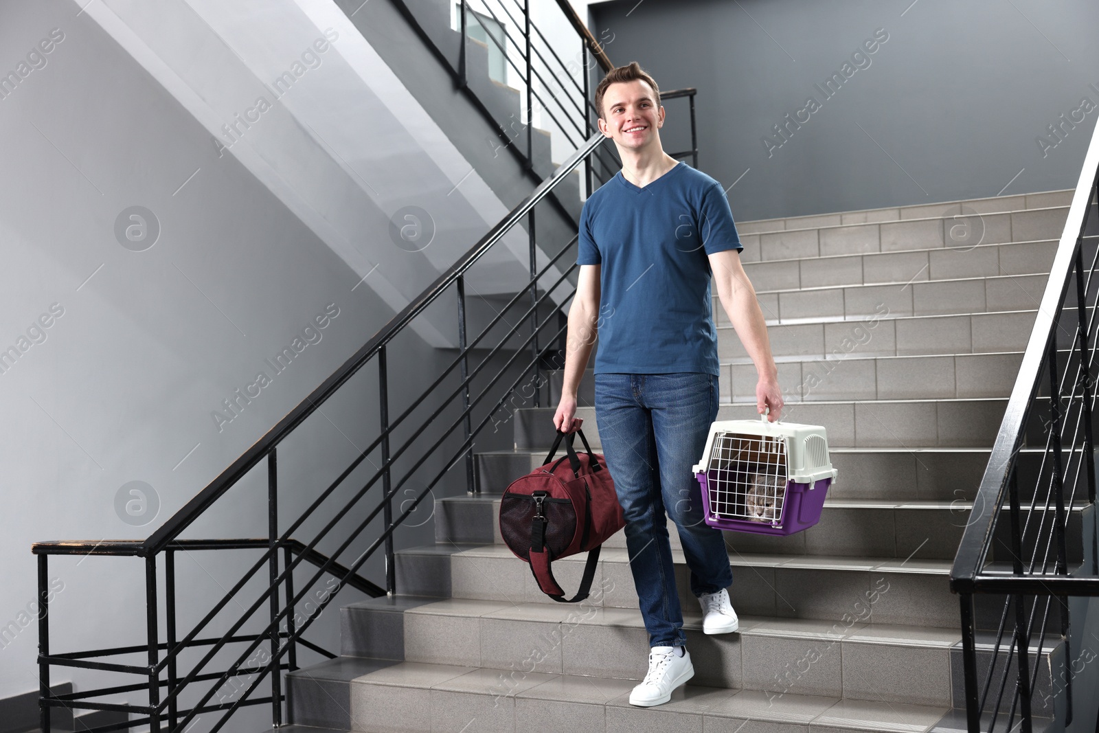 Photo of Travel with pet. Man holding carrier with cute cat and bag on stairs indoors